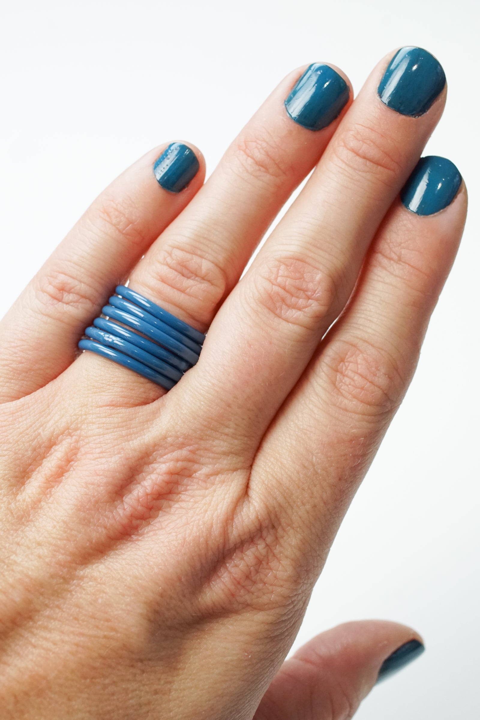 hand wearing azure blue stacking rings and matching nail polish